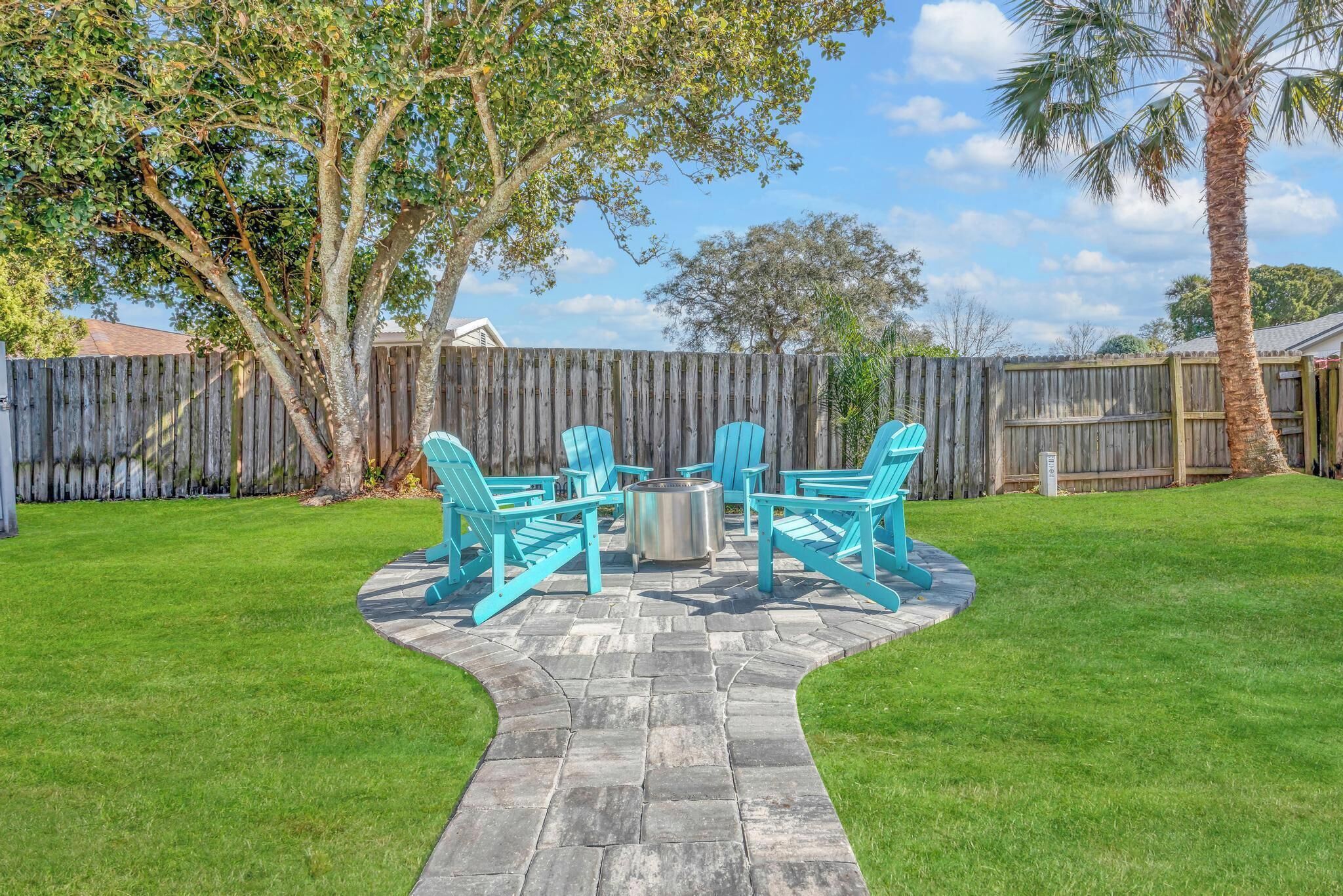 A patio area with a stone pathway, turquoise chairs, and a metal table.