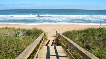 A wooden boardwalk leading to a beach with ocean waves in the background.