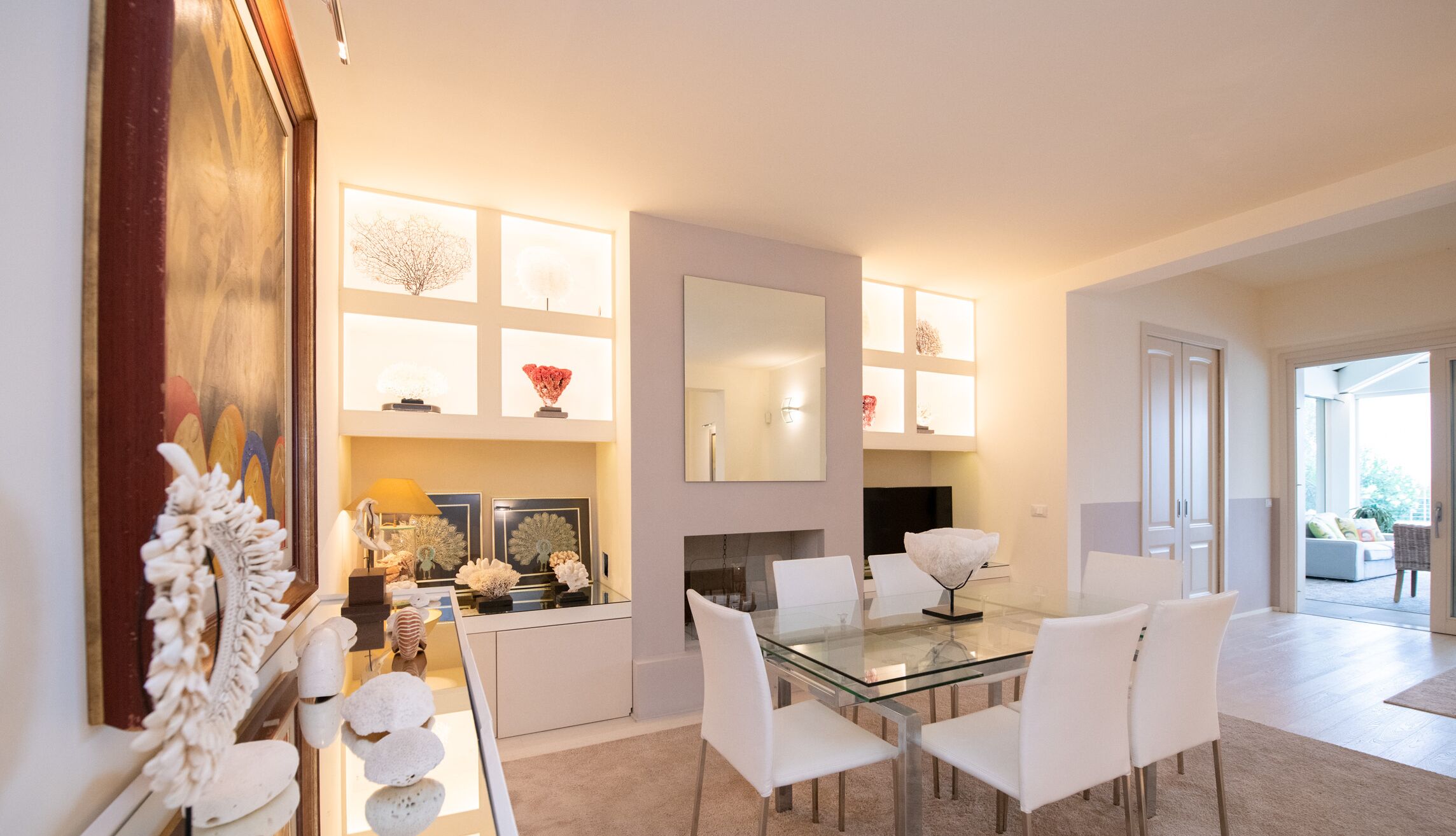 A modern dining area with a glass table, white chairs, and decorative items on shelves.
