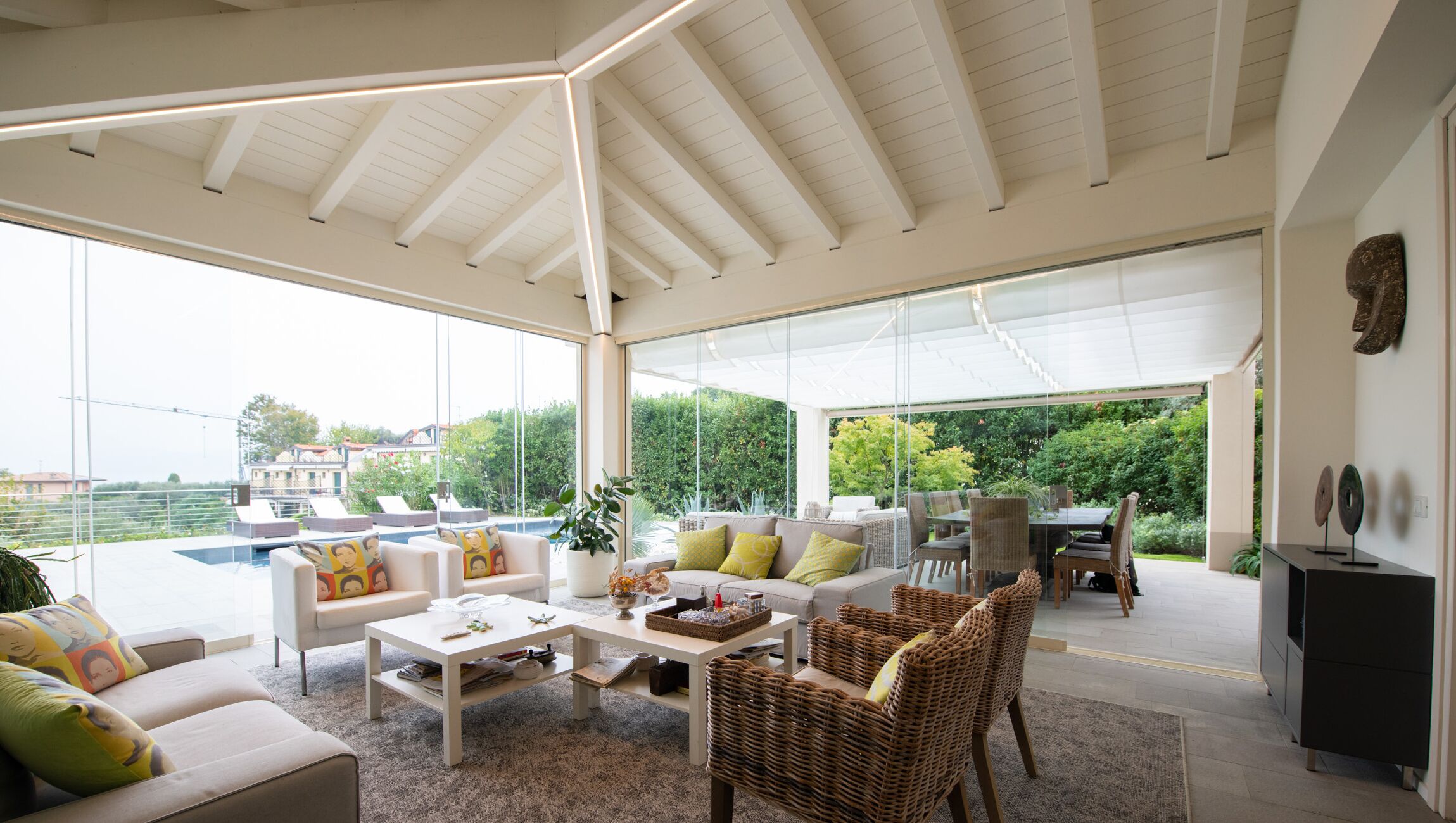 A spacious living area with a large glass wall, a pool, and outdoor seating.