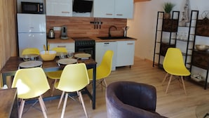 A compact kitchen with white cabinets, a microwave, a coffee maker, and a dishwasher. There are yellow chairs around a dining table.