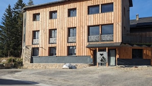A modern wooden building with multiple windows and balconies, stone foundation, and a gravel driveway.