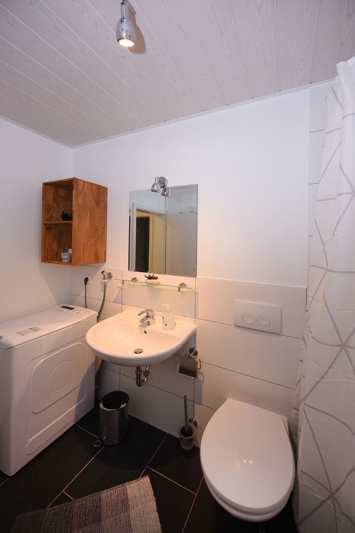 Une salle de bain moderne avec un lavabo, un miroir et des toilettes blancs. On y trouve également un meuble en bois et un lave-linge.