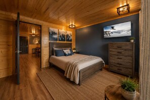 A wooden cabin bedroom with a bed, a dresser, a painting, and a television. - Mountain Views at Dolly's Castle 2 (Sevierville)