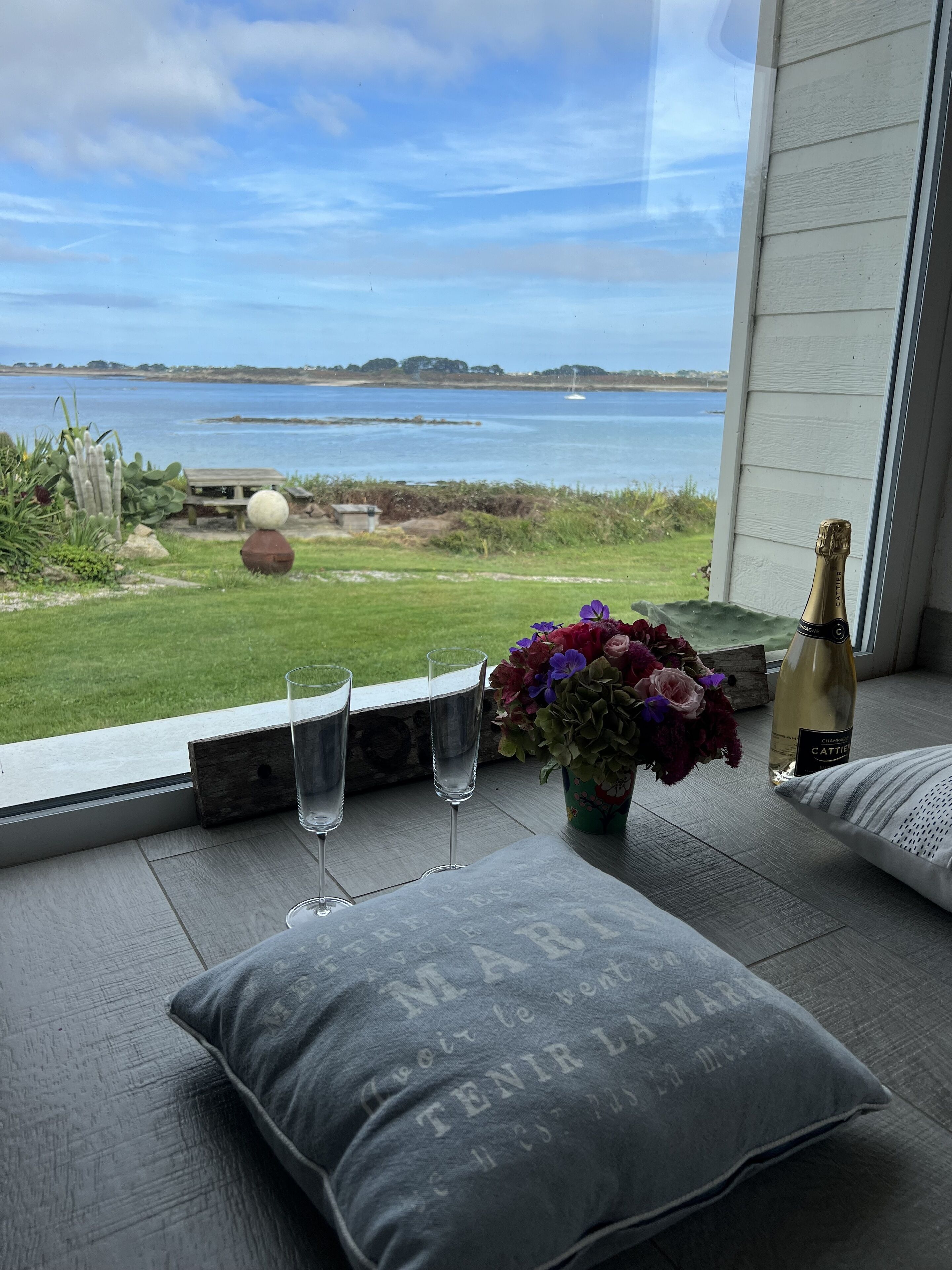 Een balkon met uitzicht op zee, een fles champagne en een bloevas.