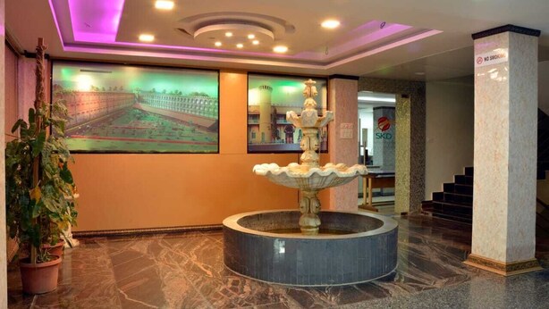 A lobby with a marble floor, a fountain, a large wall mural, and a staircase. - Sree Karpagam Dreams (Port Blair)