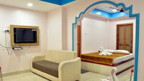 A hotel room with a sofa, a bed with towels, a television, and a mirror. - Sree Karpagam Dreams (Port Blair)