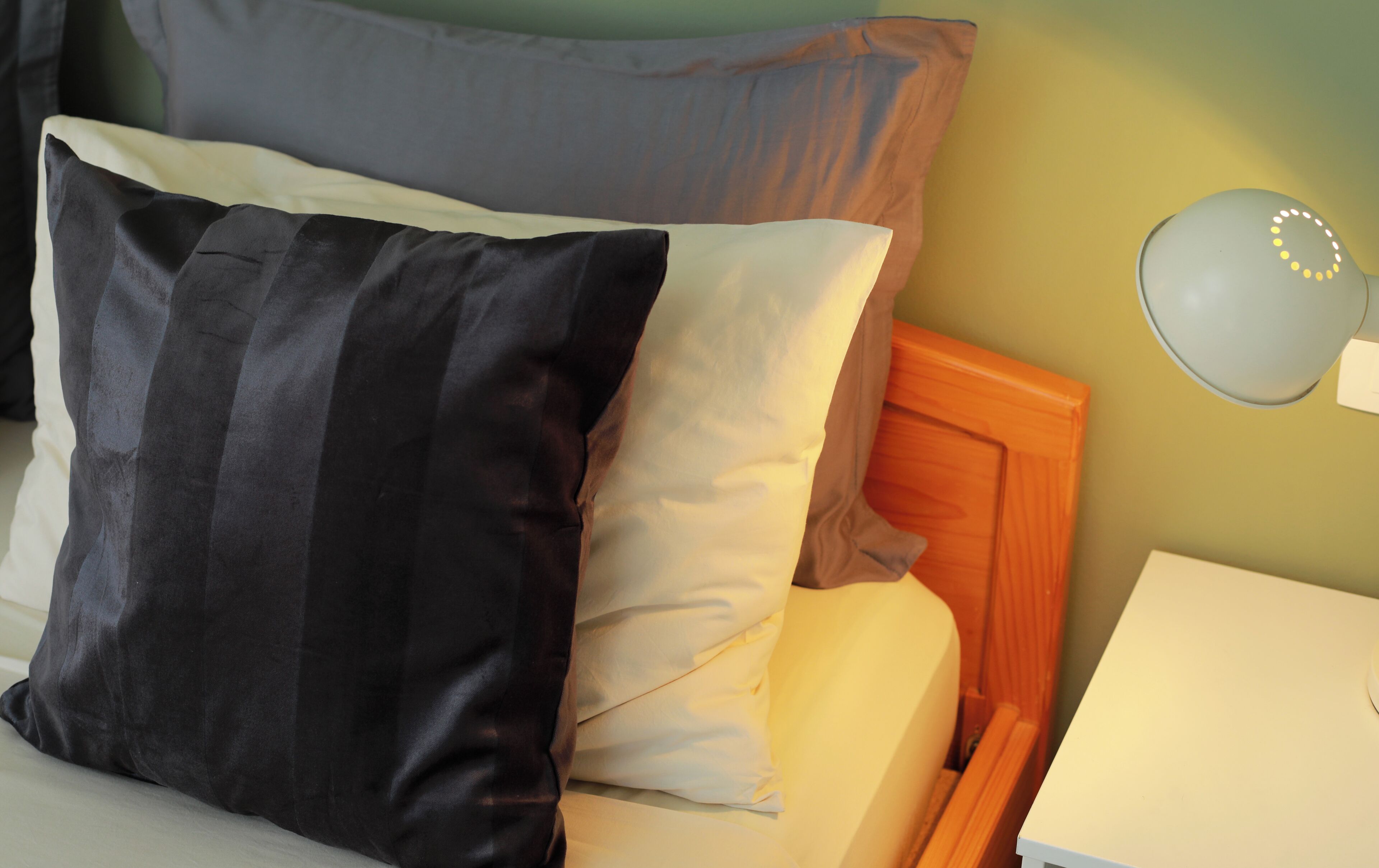 A bed with two pillows, a bedside table, and a wall-mounted lamp.