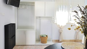 Une pièce avec un téléviseur fixé au mur, une armoire, un panier en osier et une fenêtre avec des rideaux.