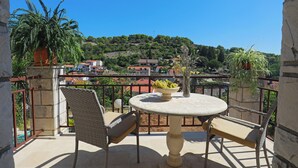 Un balcon avec des fauteuils en osier, une table ronde sur laquelle se trouve un saladier rempli de fruits et des plantes en pot.