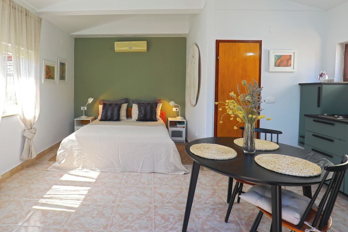 A hotel room with a bed, bedside tables, a desk, a chair, a vase with flowers, and a door.