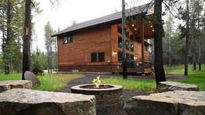 A wooden cabin with a fire pit in the center, surrounded by large rocks.