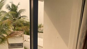 A narrow balcony with a tiled floor, a white wall, and a palm tree in the background.