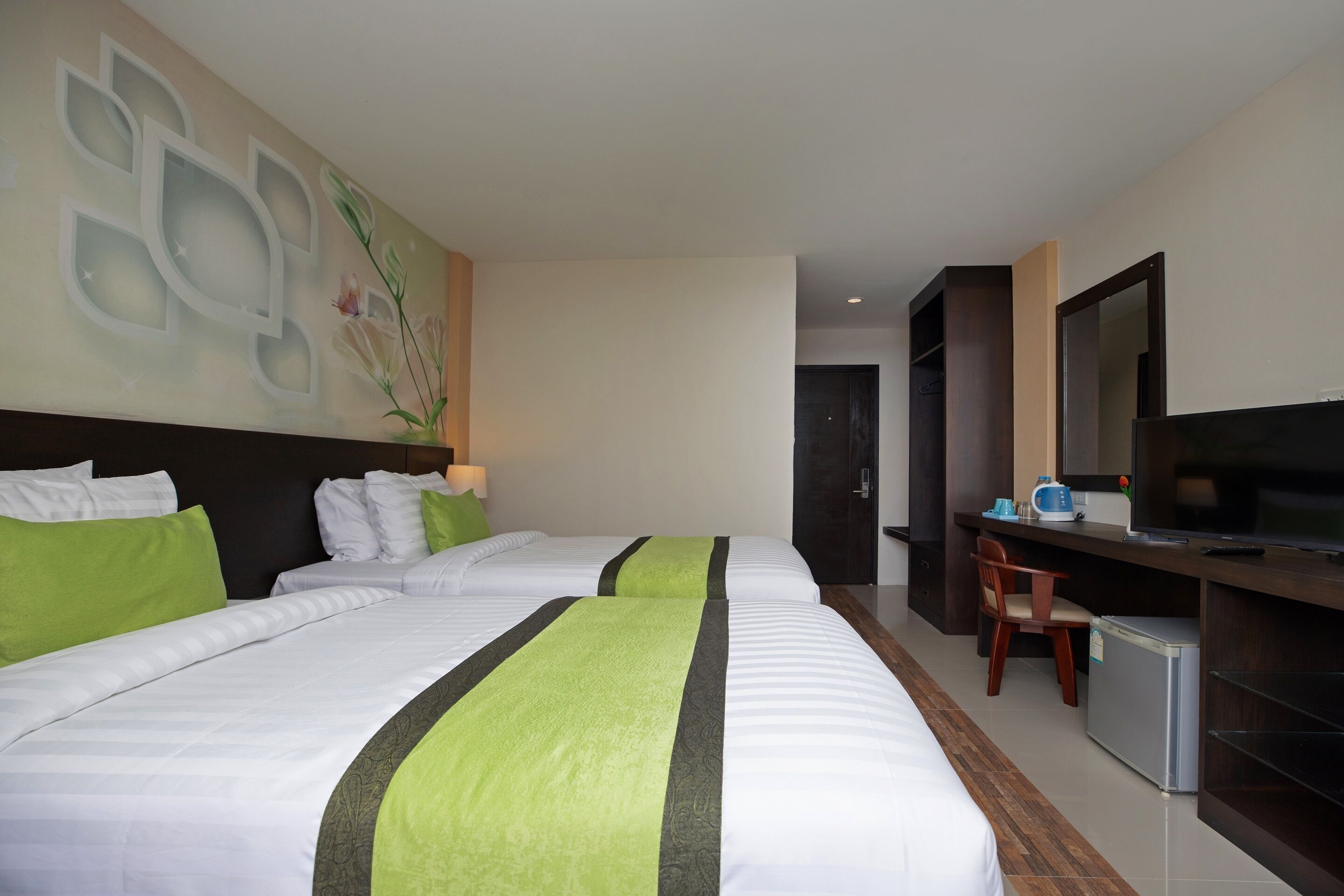 A hotel room with two beds, a desk with a television, and a small refrigerator.
