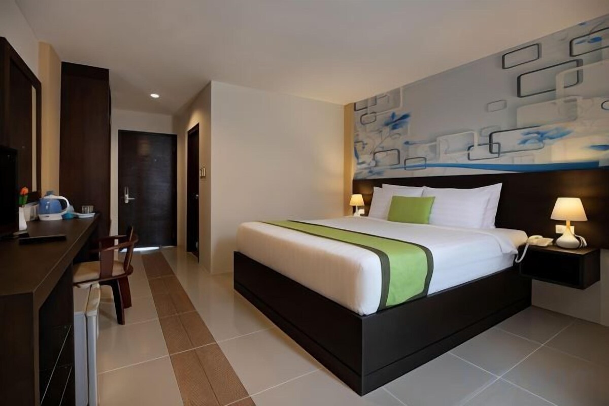 Una habitación de hotel con una cama grande, mesitas de noche, un escritorio y una silla.
