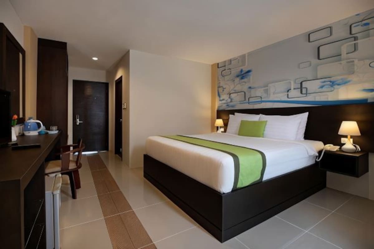 A hotel room with a large bed, bedside lamps, a desk with a chair, and a modern abstract wall art.