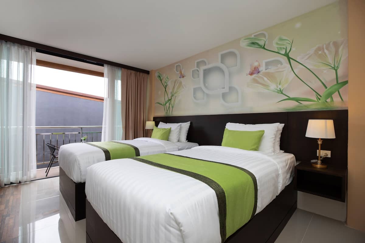 A hotel room with two beds, a balcony with a view, and a wall with a floral mural.
