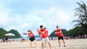 Una playa con gente vestida de camisetas rojas y pantalones cortos blancos, algunos de pie y otros sentados en sillas.
