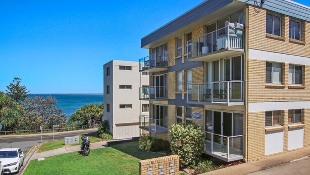 Um prédio de apartamentos com várias andares, varandas, vista para o mar e um gramado bem cuidado.