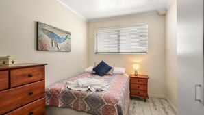 Quarto com cama, penteadeira, mesa de cabeceira, luminária, janela com persianas e um quadro pendurado na parede.
