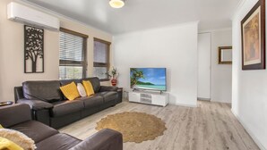 Sala de estar com sofá cinza, televisão de tela plana e piso de madeira.