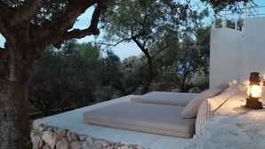 A stone bench with cushions, a lantern, and a view of trees and a building in the background.