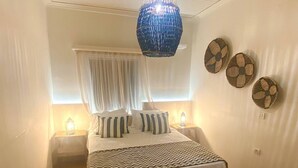 A bedroom with a bed, two bedside lamps, a hanging blue light fixture, and three wall decorations.