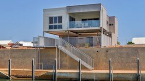 A modern two-story waterfront building with a balcony, a staircase, and a concrete foundation. - 22 Cooyou Close - Perfect Little Get Away (Exmouth)