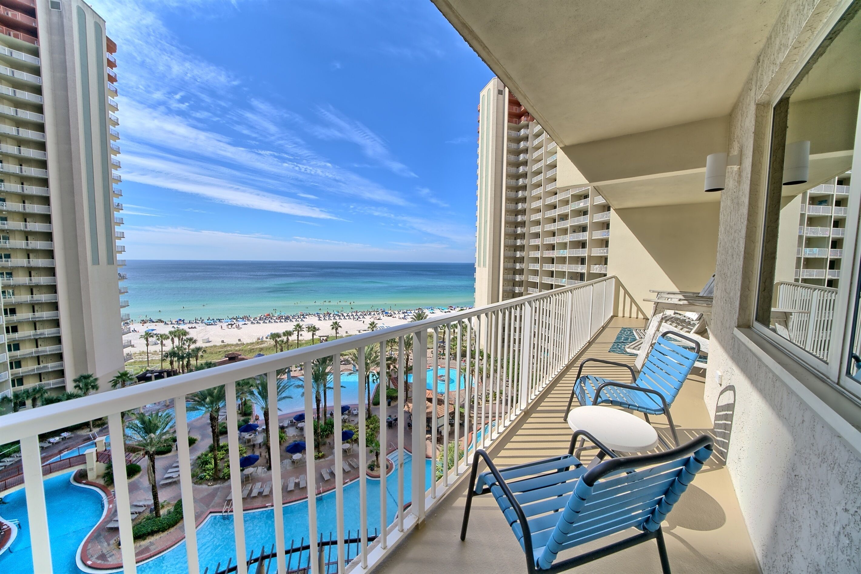A balcony with a pool, chairs, and a view of the beach and ocean.