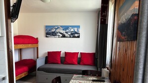 Una stanza accogliente con un letto a castello, un divano con cuscini rossi, un tavolo con una tovaglia festiva e un quadro che raffigura un paesaggio montano.