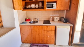 A compact kitchen with wooden cabinets, a microwave, a sink, a kettle, and a small refrigerator. - Skarinou Village Poolside Escape Studio (Skarinou)