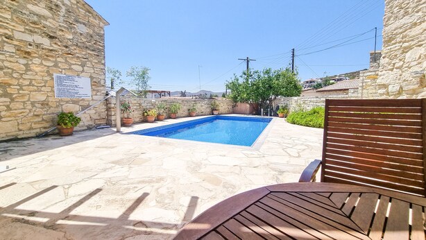 A stone-walled outdoor area with a swimming pool, potted plants, and a wooden bench. - Skarinou Village Poolside Escape Studio (Skarinou)