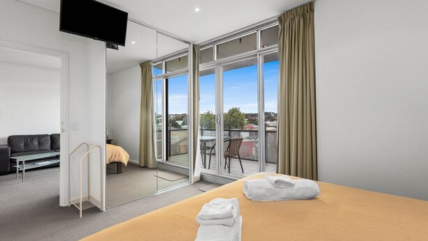 Habitación de hotel moderna con una cama grande, un sofá, un televisor y un balcón con vistas a la ciudad.