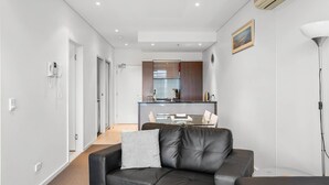 Una sala de estar moderna con un sofá de cuero negro, una mesa de centro de vidrio y una zona de comedor con una mesa y sillas blancas.