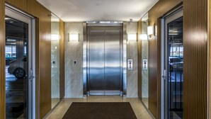 Un ascensor moderno con acabado metálico, flanqueado por paneles de madera y puertas de vidrio.