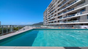 A modern hotel with a rooftop pool, multiple balconies, and a view of the sea.