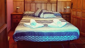 Quarto com cama de madeira, duas mesinhas de cabeceira, um candelabro e um aplique na parede.