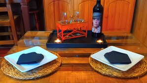 Uma mesa de jantar com dois pratos quadrados, uma garrafa de vinho, copos e uma vela.