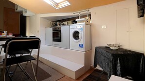 Una cocina compacta con lavadora y secadora integradas, un comedor con mesa y sillas, y una mesita con una cesta.
