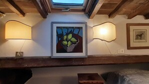 Una habitación con tragaluz, un cuadro con una planta y dos lámparas fijadas a la pared.