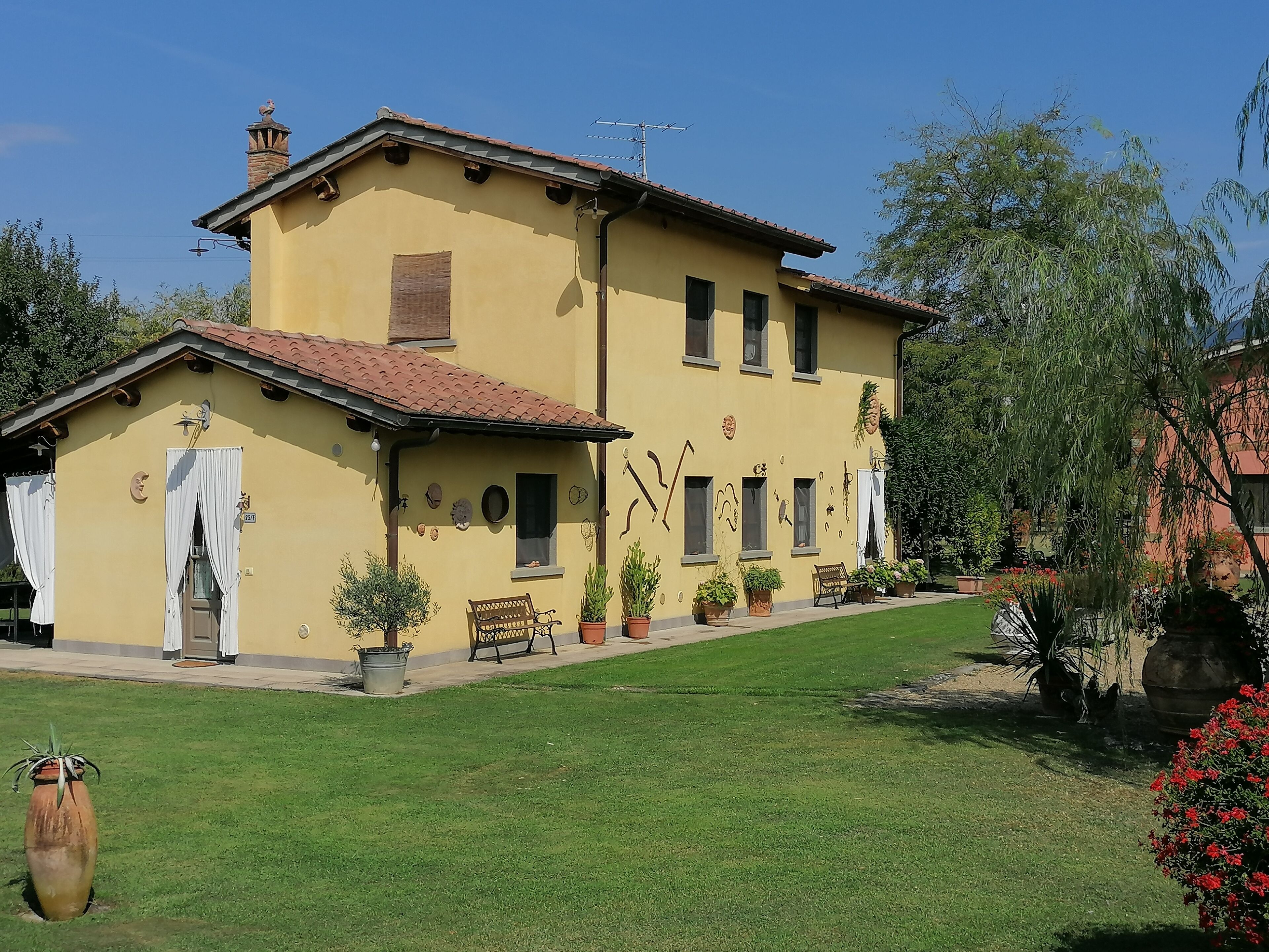 A two-story yellow building with a tiled roof, multiple windows, and a small porch area with a bench.