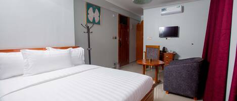 Habitació d'hotel amb un llit gran, una taula petita, una cadira, un televisor i un ventilador de sostre.