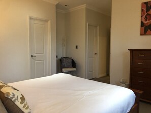 A bedroom with a bed, a chair, a dresser, and two doors. - Location, Location! Huge beachside house, 5 min walk to coffee shop and town! (Beachlands)