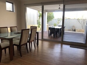 A dining area with a glass table and chairs, a sliding glass door leading to an outdoor patio with a table and chairs. - Location, Location! Huge beachside house, 5 min walk to coffee shop and town! (Beachlands)