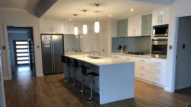 Una cucina moderna con isola centrale, sgabelli da bar, elettrodomestici in acciaio inossidabile e mobili bianchi.