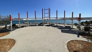 Un vialetto lastricato conduce a una piattaforma panoramica con una scala, affacciata su una zona costiera sotto un cielo sereno.