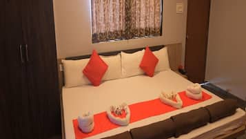 A neatly made bed with red and white pillows, a red blanket, and a set of towels on a red mat.