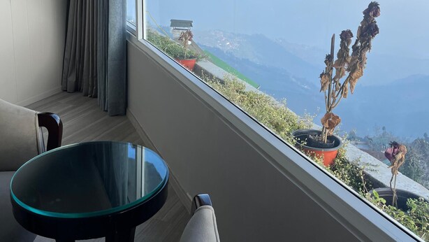 A balcony with a view of snow-capped mountains, a glass table, and a chair. - The Retreat (Darjeeling)