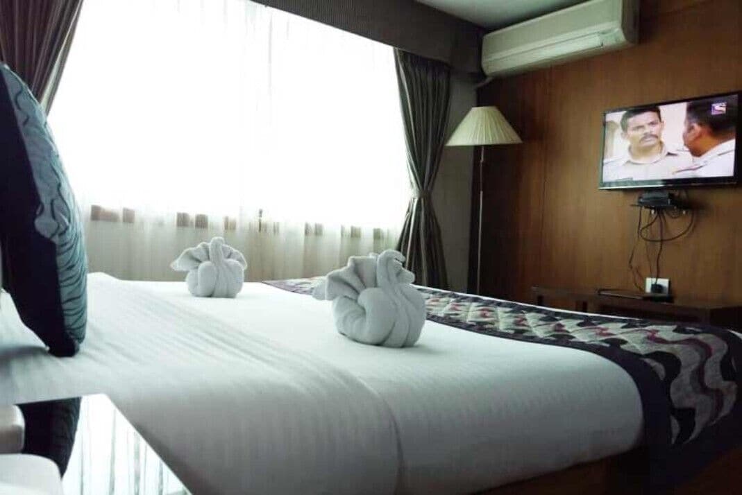 A hotel room with a bed, two towels, a television, and a window with curtains.