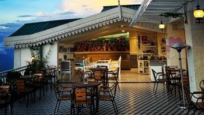 An outdoor seating area with tables and chairs, a patterned floor, and a building with a green roof and decorative elements. - The Retreat (Darjeeling)